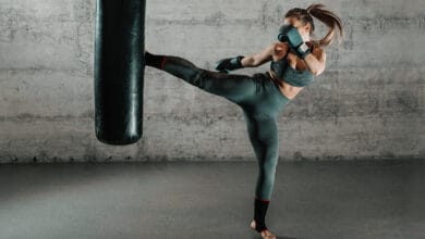 caucasian,woman,in,sportswear,and,with,boxing,gloves,kicking,bag