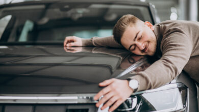 young handsome man hugging a car in a car showroom
